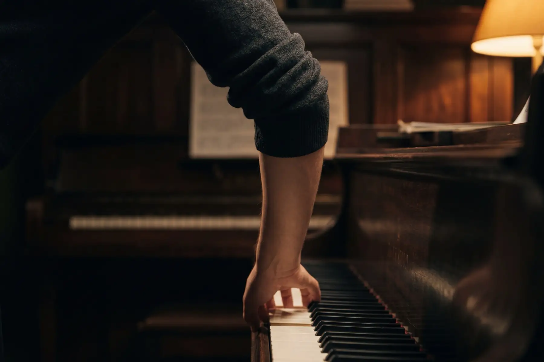 A forearm descending vertically to a piano keyboard in warm amber lamplight — the arm's weight and trajectory as the foundation of rhythmic control