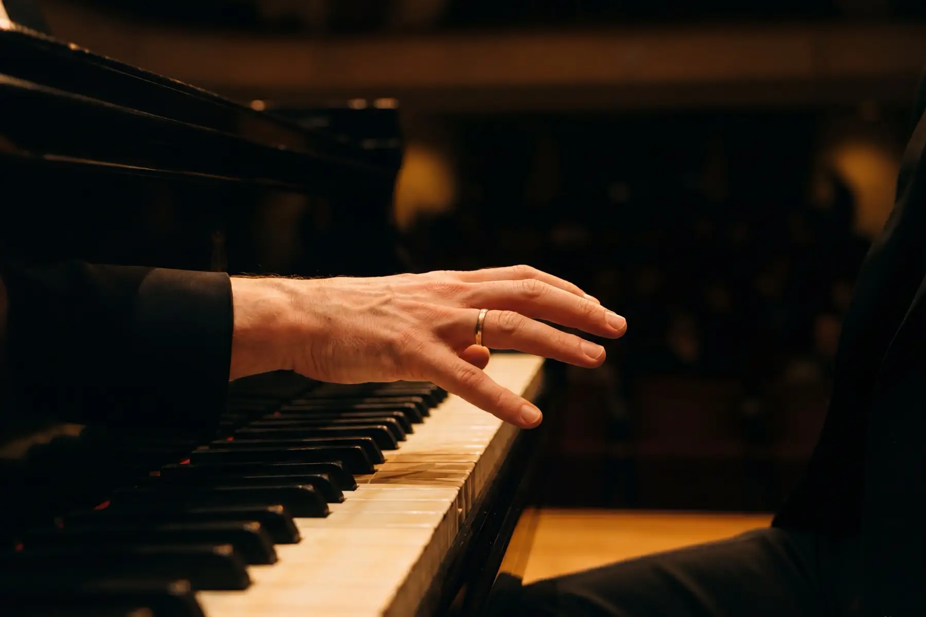 A single candle flame illuminates the nearest piano keys in near-total darkness, a warm breakthrough after patient practice